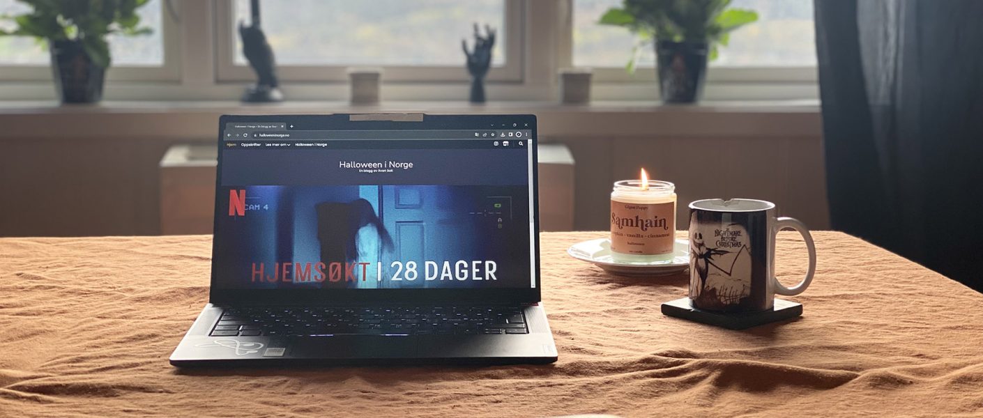 Bord med laptop, talgelys og kaffekopp. Halloween dekor i bakgrunnen.