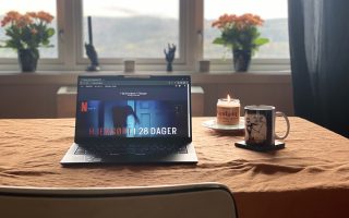 Bord med laptop, talgelys og kaffekopp. Halloween dekor i bakgrunnen.