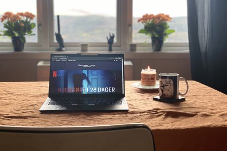 Bord med laptop, talgelys og kaffekopp. Halloween dekor i bakgrunnen.