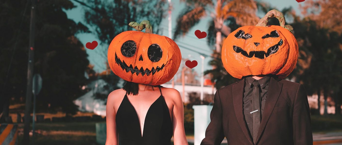 Valloween par. Kjærester holder hender. Har på seg utskjærte gresskar hoder.
