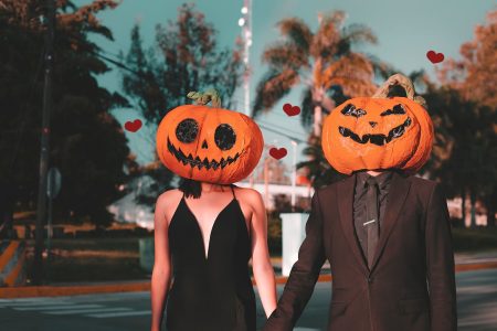 Valloween par. Kjærester holder hender. Har på seg utskjærte gresskar hoder.